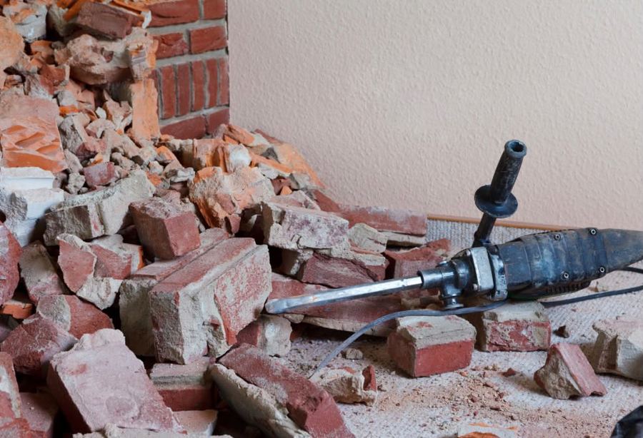 Abgebrochene Ziegelwand im Innenraum mit Haufen aus Mauersteinen und ein abgelegter Bohrhammer mit Meißel.