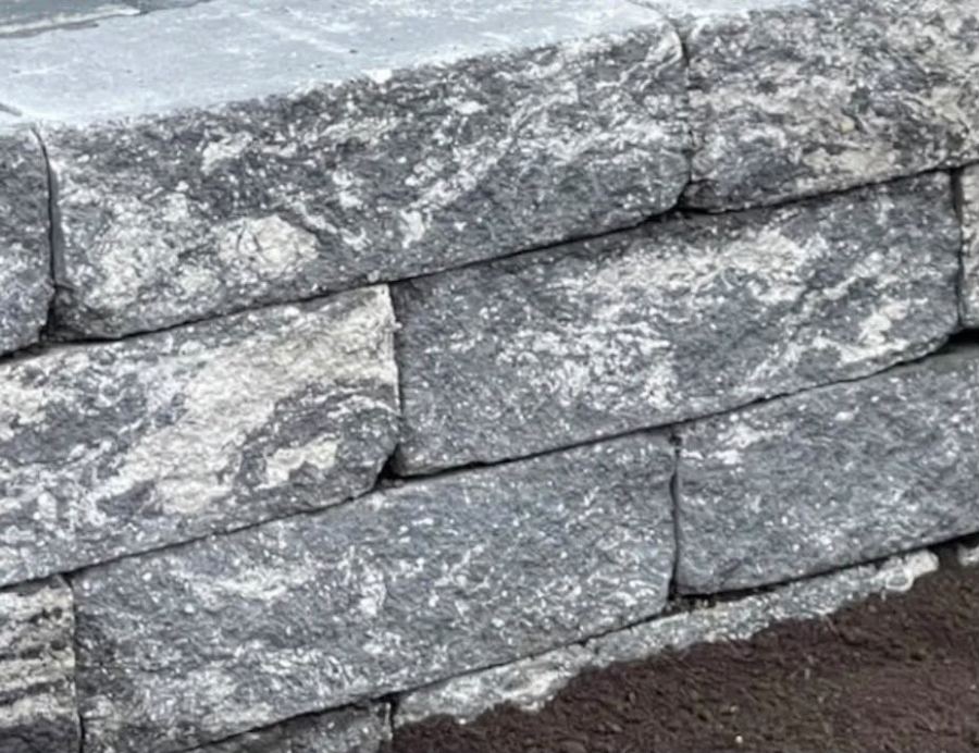 Nahaufnahme einer gesetzten Natursteinmauer aus grauen Granitblöcken mit abschließender Deckplatte.