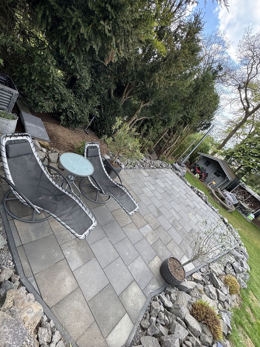Neu gepflasterte Gartenterrasse mit Natursteineinfassung, Liegestühlen und Gartenblick (schräger Bildwinkel).