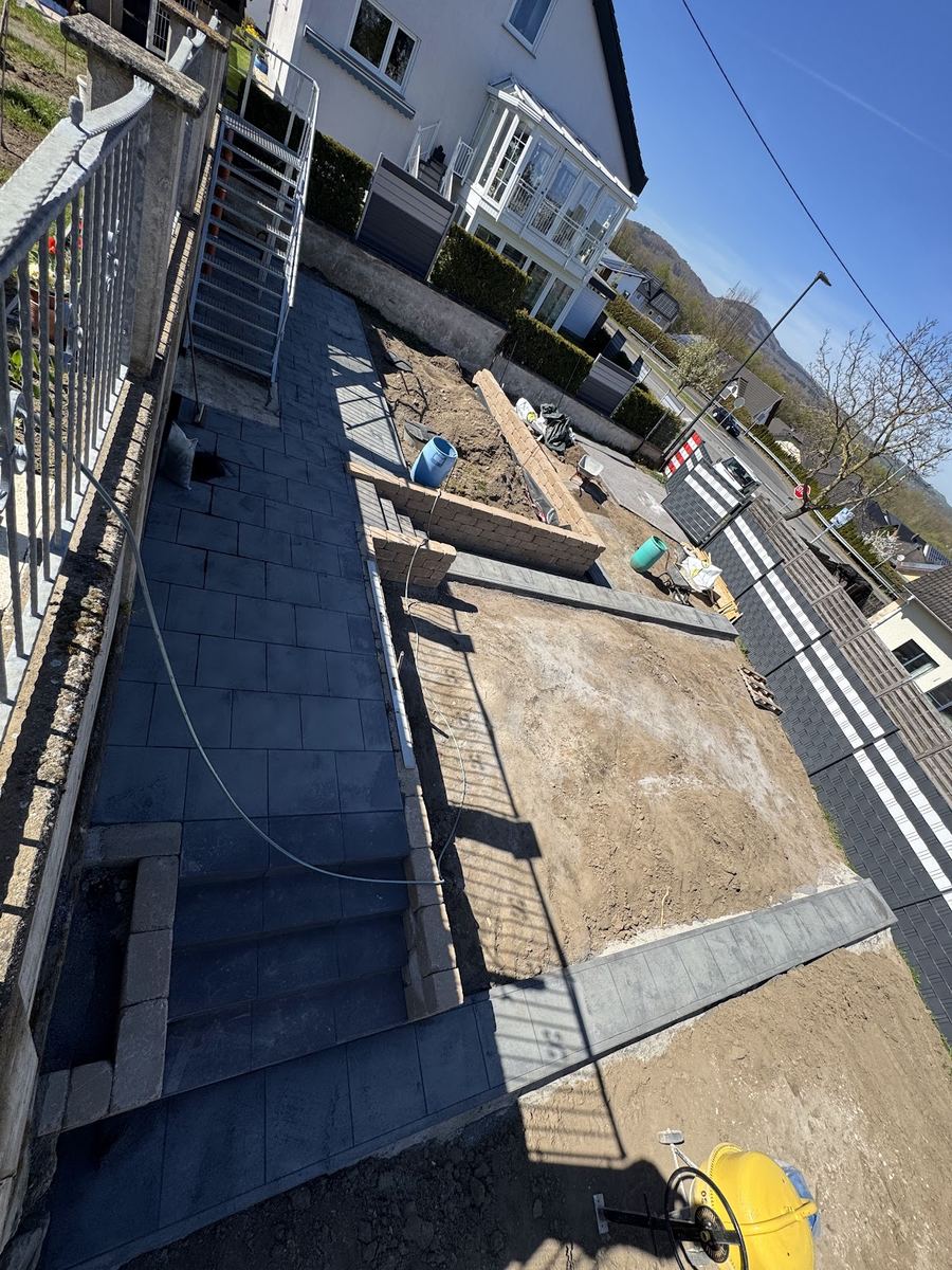 Neu angelegte dunkle Pflasterterrasse mit Treppenstufen und Mauersteinen, Außenanlage noch im Bau.